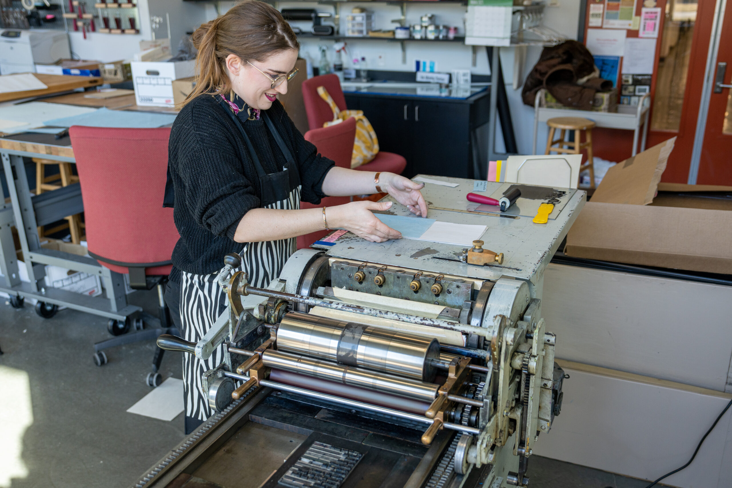 Image of student working on her creation in the letterpress studio using one of the machines.