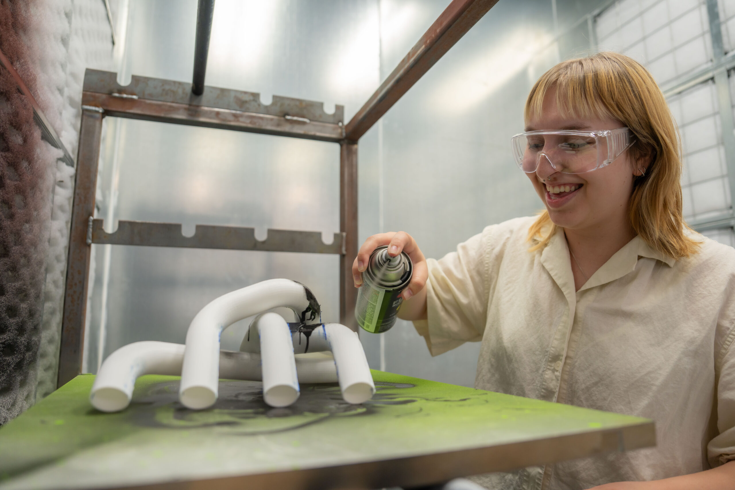 Image of a student spray painting her latest project inside the paint booth.